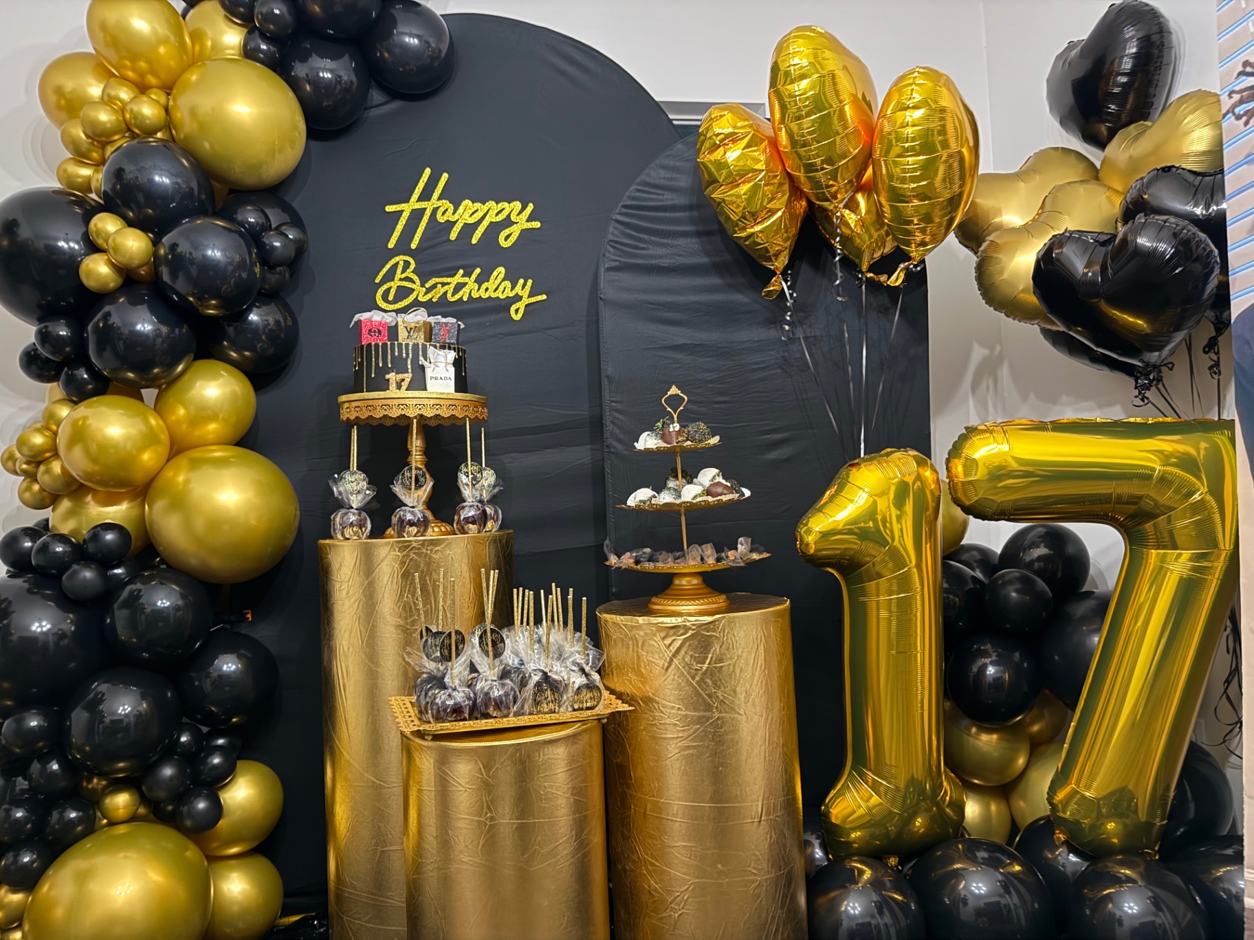 Black and gold 17th birthday dessert table with balloon arch